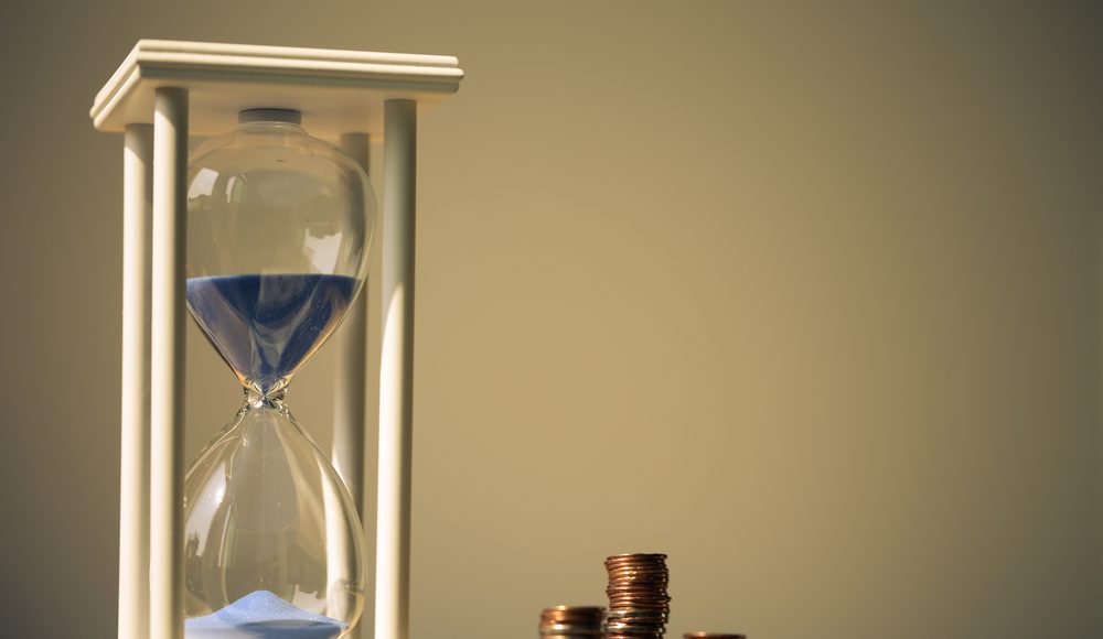 Close,Up,Shot,Of,Hourglass,And,Coins,With,Blank,Background.
