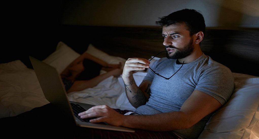 Modern,Workaholic-man,Lying,On,Bed,At,Home,And,Working,With