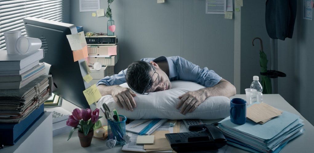 Exhausted,Businessman,Sleeping,At,Workplace,With,A,Pillow,On,His